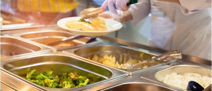 in a school canteen, a person wearing a white shirt serves food